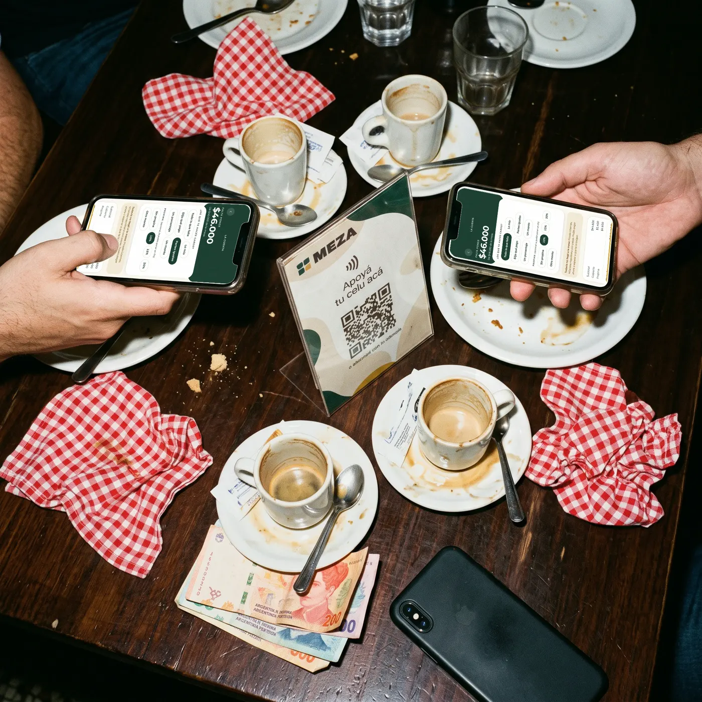 Dos personas ven la cuenta en su teléfono para pagar cada una su parte, en la mesa de un bodegón